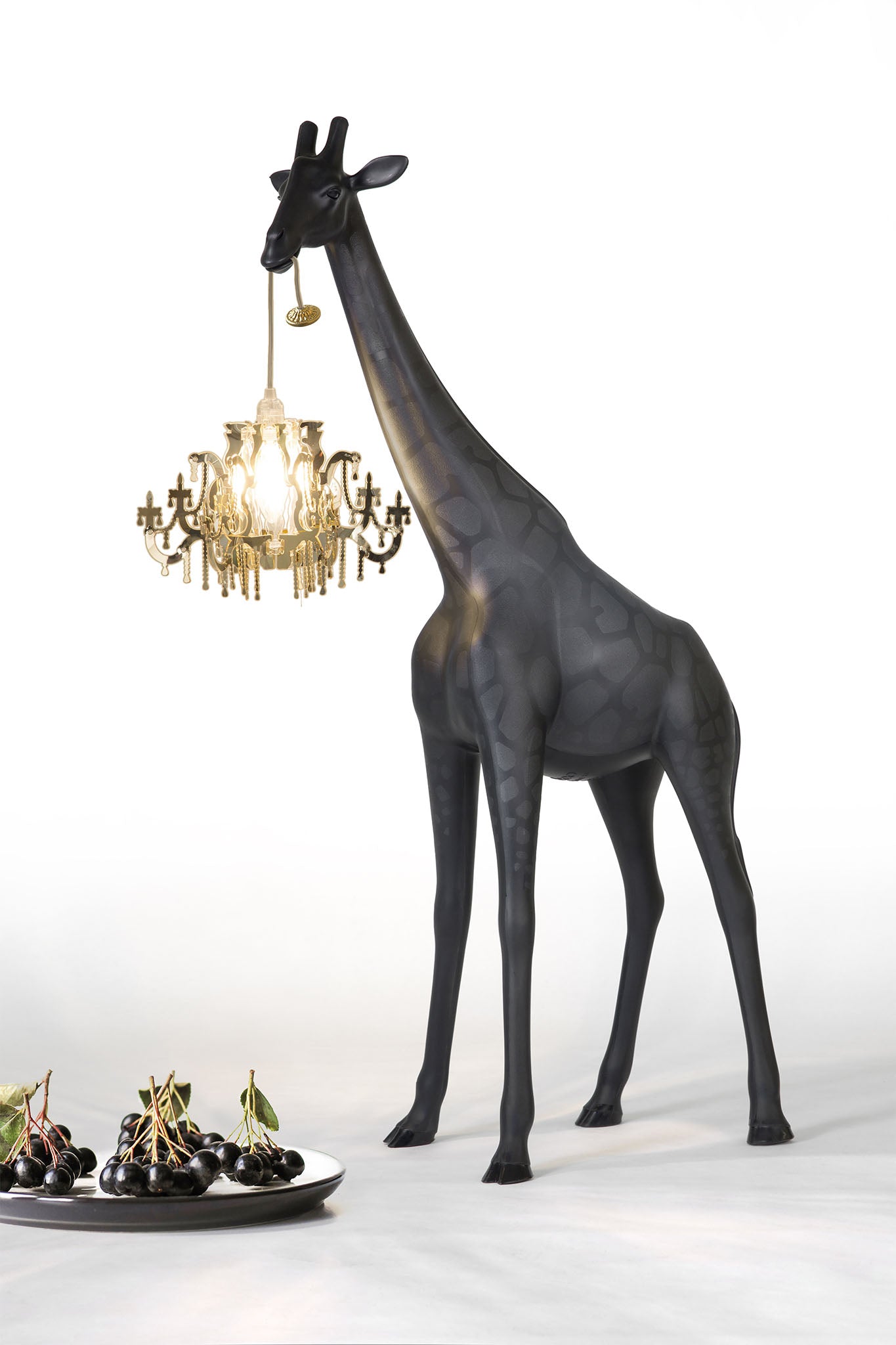 Stehleuchte GIRAFFE IN LOVE XS in schwarz mit Kronleuchter vor einem Teller mit Kirschen