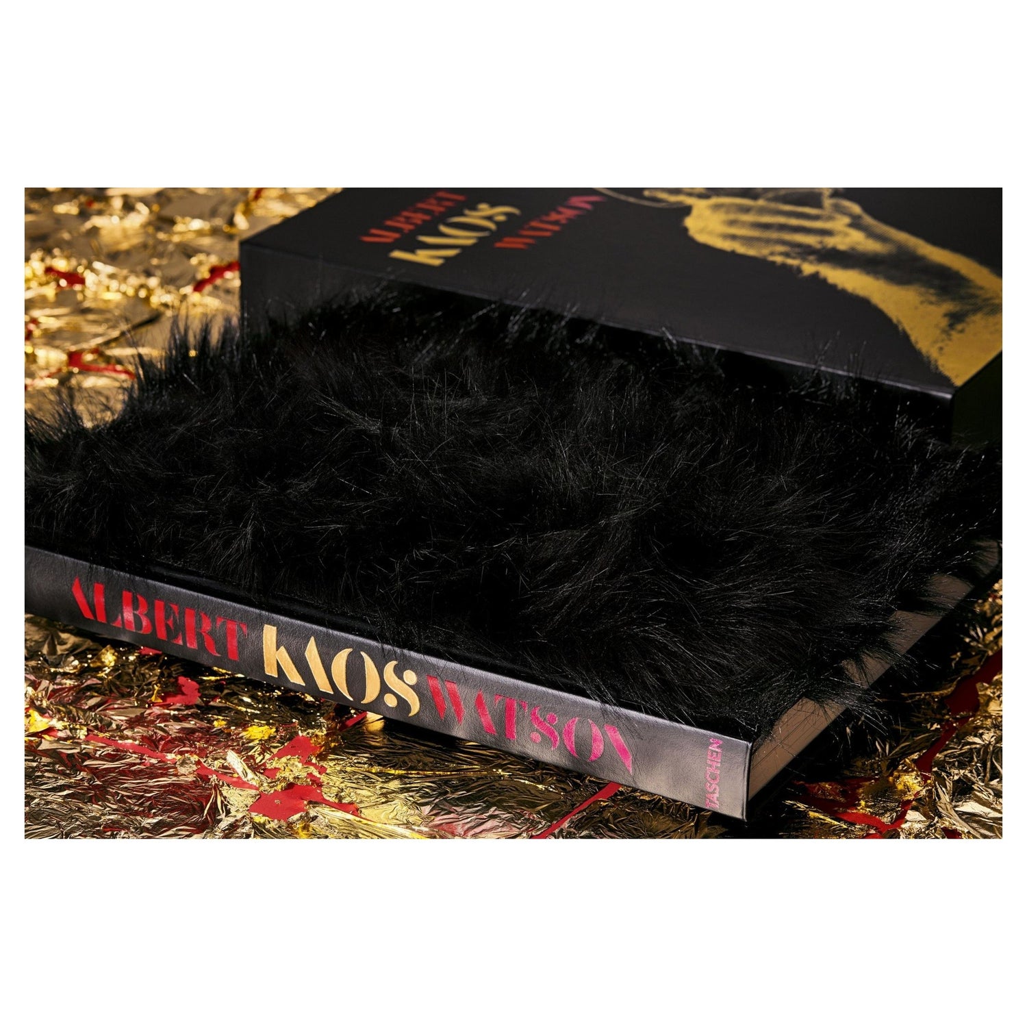 Goldfoliertes Hintergrunddesign mit markanten Strukturen neben dem KAOS Buch.